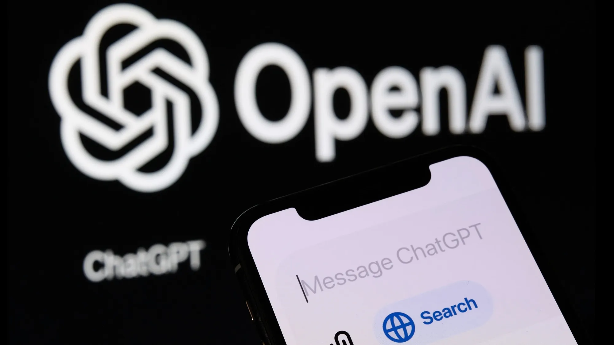 A smartphone showing the ChatGPT message input screen, in front of a dark background bearing the OpenAI logo